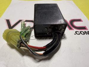 Black rectangular electrical part with multiple colored wires and a yellow connector, resting on a white surface with pink letters in the background.
