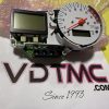Disassembled car tachometer gauge cluster with orange needle, two digital displays, and exposed circuit board on a pink bubble wrap background.