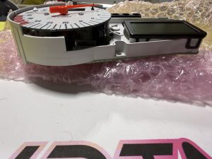 Close-up of a circular analog timer dial with a red pointer on a white housing, next to an LCD screen on the right.