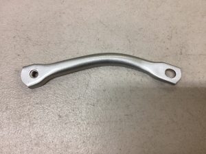 Curved silver metal lever with a small threaded hole at one end and a larger round hole at the other, lying on a gray surface