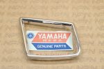 Chrome rectangular frame badge with a Yamaha Genuine Parts sticker showing the Yamaha logo and text 'Genuine Parts'.