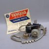 Yamaha Genuine Parts label beside a metal motorcycle electrical component with bolts and gears on a gray surface.