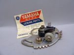 Yamaha Genuine Parts label beside a metal motorcycle electrical component with bolts and gears on a gray surface.