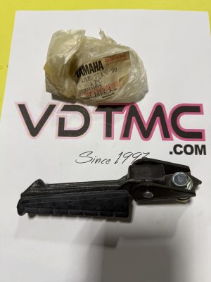 Crinkled plastic bag with a Yamaha Genuine Parts label sits on a white surface with pink lettering; a black motorcycle footpeg is in view nearby.