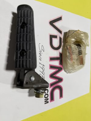 Close-up of a black handgun grip with textured surface and metal hardware on a white and yellow background, with a crumpled plastic-wrapped paper nearby.