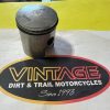 Piston resting on a Vintage Dirt & Trail Motorcycles logo mat with Since 1993 text.