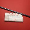 Long metal bolt with threaded ends lying diagonally on a red surface, partly covering a white contents label.