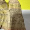 Crinkled brown paper bag with printed black text, standing on a light surface against a bright yellow background.