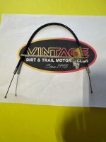 Braided motorcycle control cable with metal end fittings, laid over a Vintage Dirt & Trail Motorcycles sign.