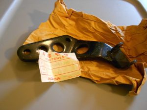 s-l1600 Black automotive bracket with multiple circular holes, lying on crumpled brown paper, with a Honda contents tag attached/nearby.
