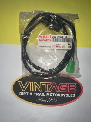 Bagged Yamaha genuine parts cable with a green connector, labeled 'YAMAHA Genuine Parts & Accessories,' on a Vintage Dirt & Trail Motorcycles backdrop.