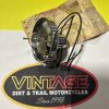 Close-up of a vintage motorcycle speedometer with cables resting on a cardboard backing above a Vintage Dirt & Trail Motorcycles logo.
