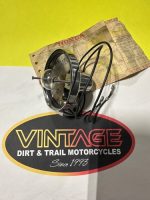 Close-up of a vintage motorcycle speedometer with cables resting on a cardboard backing above a Vintage Dirt & Trail Motorcycles logo.