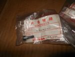 Honda parts bag labeled 'Contents' with a small black pin on a wooden surface