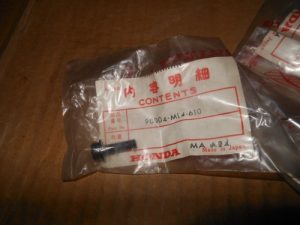 Honda parts bag labeled 'Contents' with a small black pin on a wooden surface