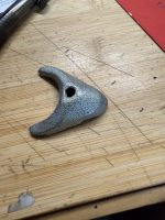 Curved metal tool with a large central hole lying on a wooden workbench surface
