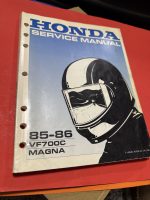 Honda service manual cover with blue gradient and motorcycle helmet illustration, 85-86 VF700C Magna edition visible on white spine set on red surface