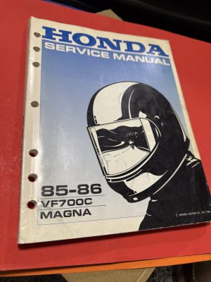 IMG_2153 Honda service manual cover with blue gradient and motorcycle helmet illustration, 85-86 VF700C Magna edition visible on white spine set on red surface