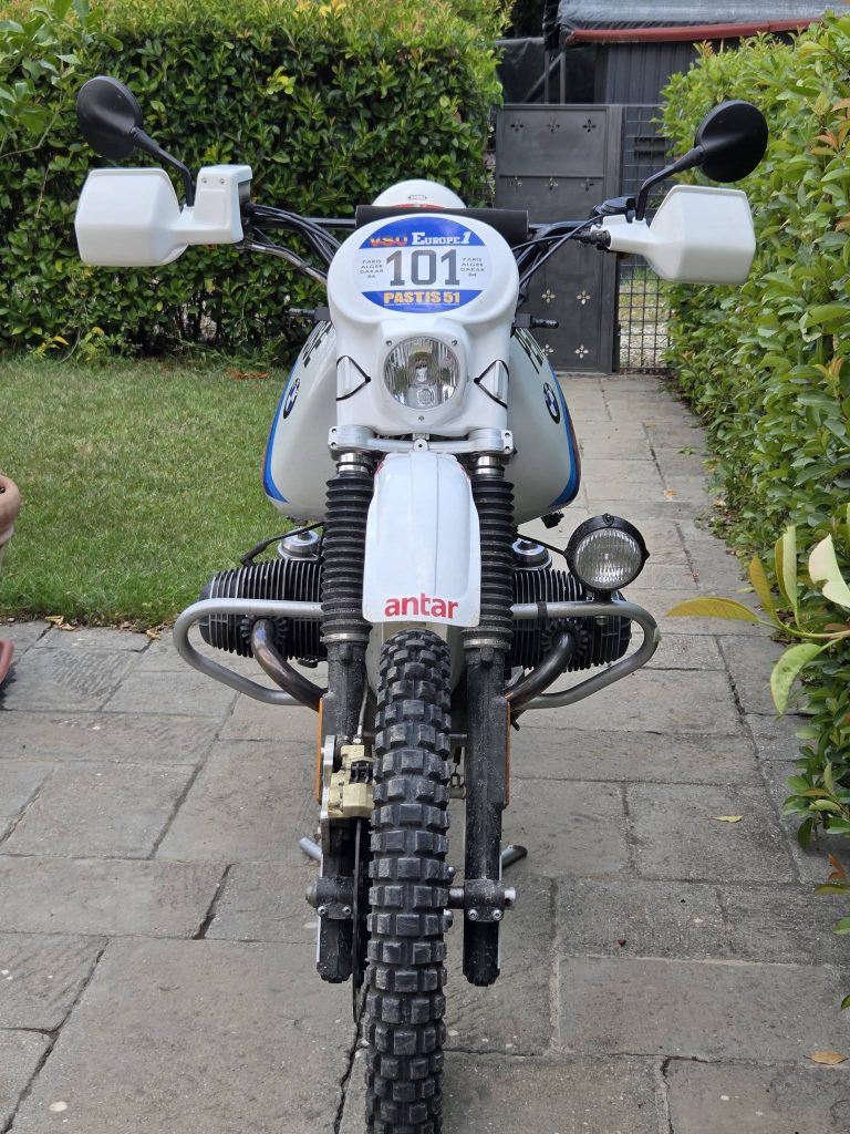 Front view of a white BMW adventure motorcycle with knobby tires, crash bars, and a plate reading 101.