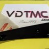 Black plastic interior car trim piece with a mounting hole, resting on a white brochure on a yellow surface, with a red sticker nearby.
