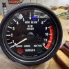 Close-up of a motorcycle tachometer face showing RPM x1000, numbers 0–12, with Yamaha branding and high-beam indicator on a workshop bench.