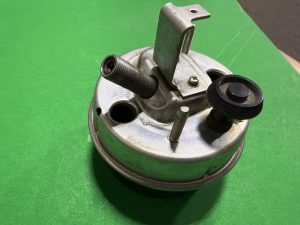 Metallic mechanical component with a threaded outlet and an adjustable knob on a green backdrop.