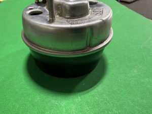 Close-up of a metal mechanical component with a threaded bolt on top, set on a bright green surface.