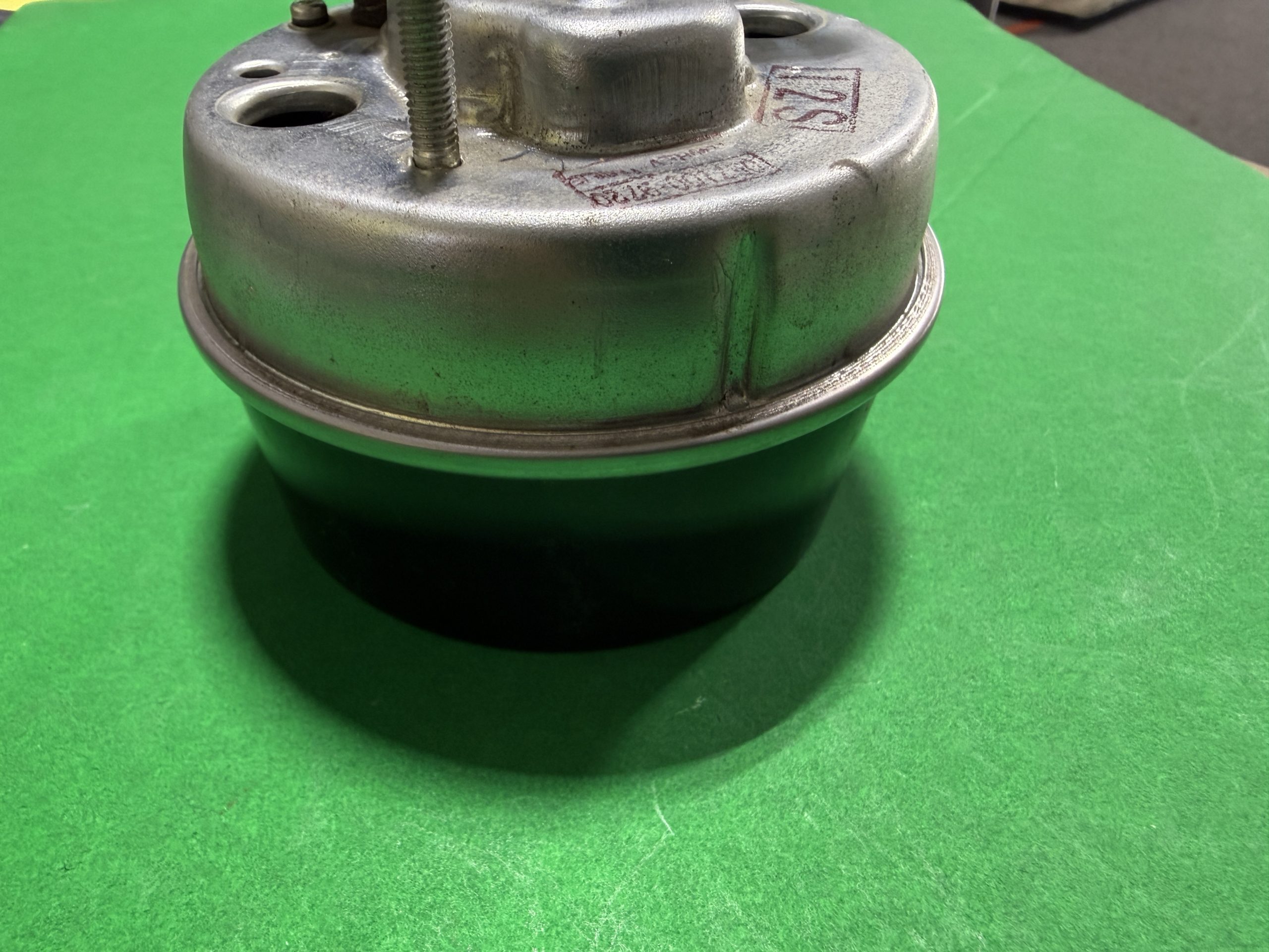 Close-up of a metal mechanical component with a threaded bolt on top, set on a bright green surface.