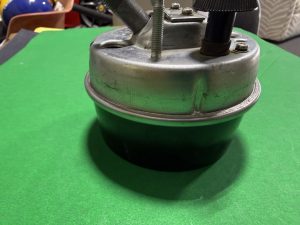 Close-up of a metal mechanical base with a threaded bolt and black adjustment knob on a green surface.
