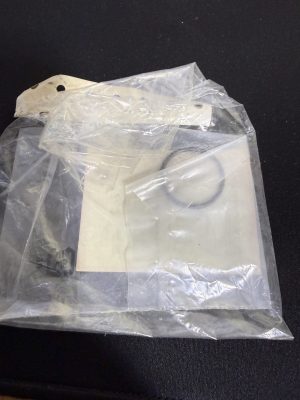 Close-up of a clear plastic bag containing white plaster or ceramic pieces with holes, resting on a dark surface.