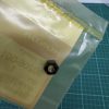 Close-up of a translucent yellow bag with a black hex nut resting on its surface, taped along a seam on a green cutting mat background.