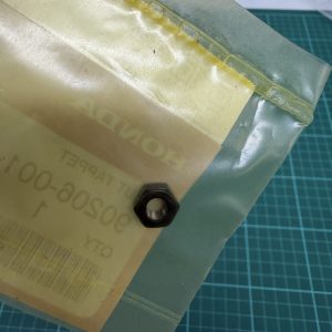 Close-up of a translucent yellow bag with a black hex nut resting on its surface, taped along a seam on a green cutting mat background.