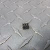 Small black helical compression spring resting on a gray diamond-plate metal surface.