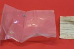Clear plastic bag on a red surface containing two small silver U‑shaped metal fasteners, with a receipt-like label to the right.