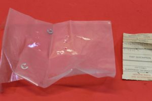 Clear plastic bag on a red surface containing two small silver U‑shaped metal fasteners, with a receipt-like label to the right.