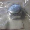 Close-up of a shiny metal cap inside clear plastic wrap on a gray surface.