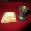 Two dark metal spur gears stacked on a short shaft, with a red fabric background and a small worn tag nearby.