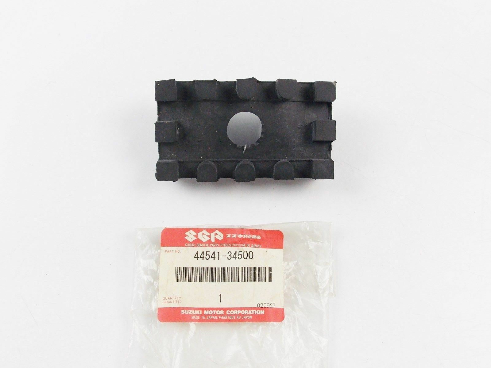 Black plastic rectangular component with raised edge tabs and a central circular hole, placed above a Suzuki genuine parts bag labeled 44541-34500.
