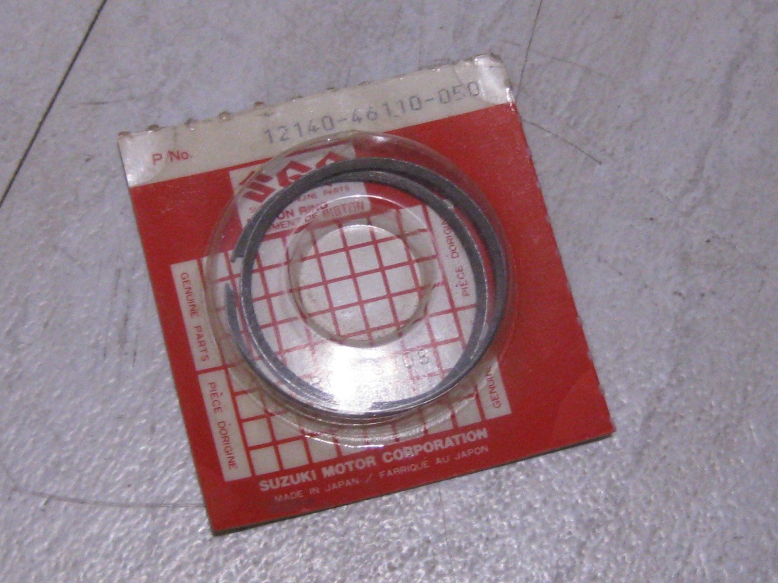 Red Suzuki motor parts packaging with a circular metal seal ring inside, Made in Japan label visible.