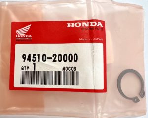 Honda genuine parts bag with red label reading 94510-20000, quantity 1,Made in Japan, plus a small circular metal retaining ring beside the bag.