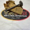 Metal engine valve resting on crumpled brown paper over a Dirt & Trail Motorcycles sign.