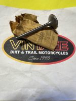 Metal engine valve resting on crumpled brown paper over a Dirt & Trail Motorcycles sign.