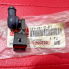 Small black plastic automotive component with a side nozzle and mounting hole on a pink textured surface, resting on a bag with a barcode label.