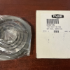 Coiled metal bearing sealed in plastic next to a white box with a barcode on a wooden surface.